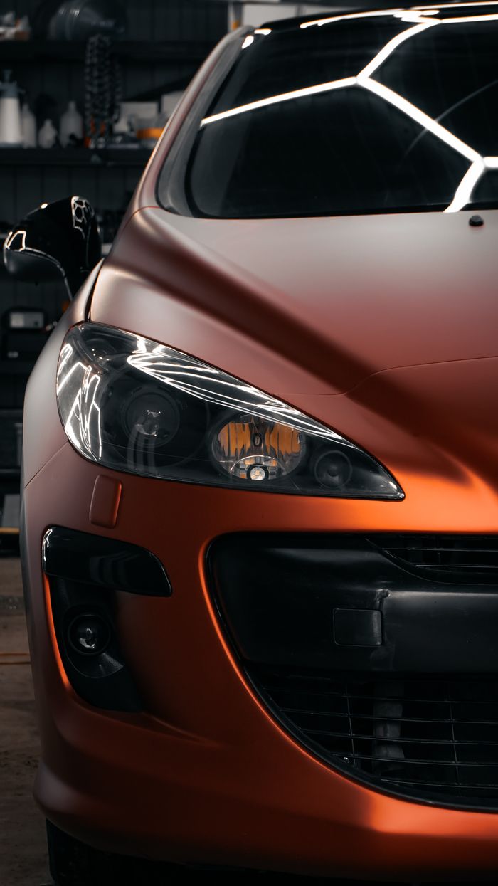 Detailed view of an orange sports car's front in a dimly lit garage, showcasing its sleek design.